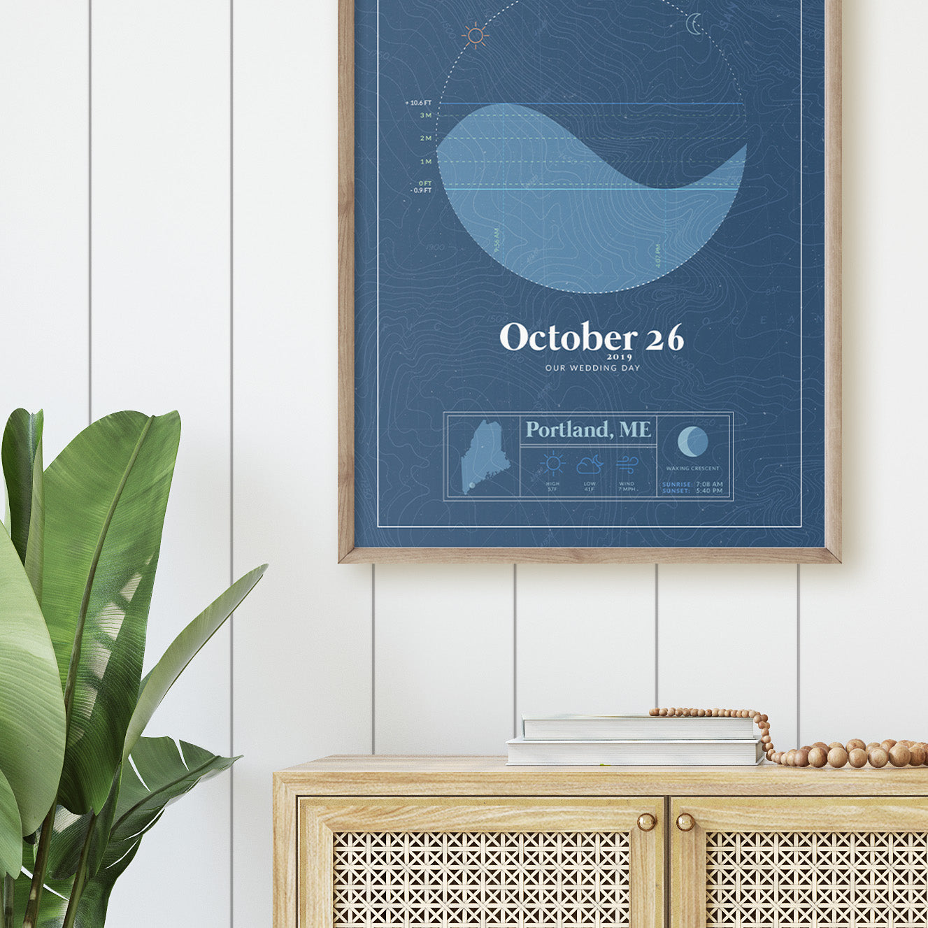close up of the wood framed picture of the personalized tide map poster by salt atlas in the vintage cobalt blue color in a home setting. These are custom posters showing the tide, weather, and moon phase for a special day, like an anniversary or birthday.